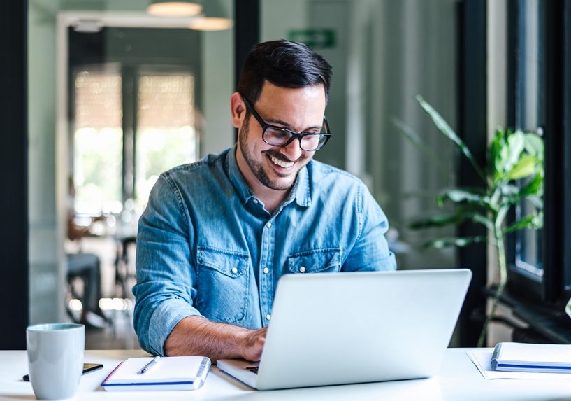 Smiling,Young,Entrepreneur,Working,On,Laptop,At,Table